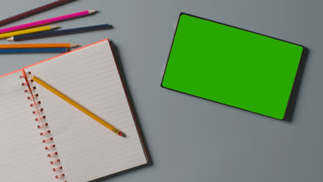 Overhead-Aufnahme-Eines-Kindes-Mit-Grünem-Bildschirm-Und-Digitalem-Tablet,-Das-In-Ein-Schulheft-Schreibt